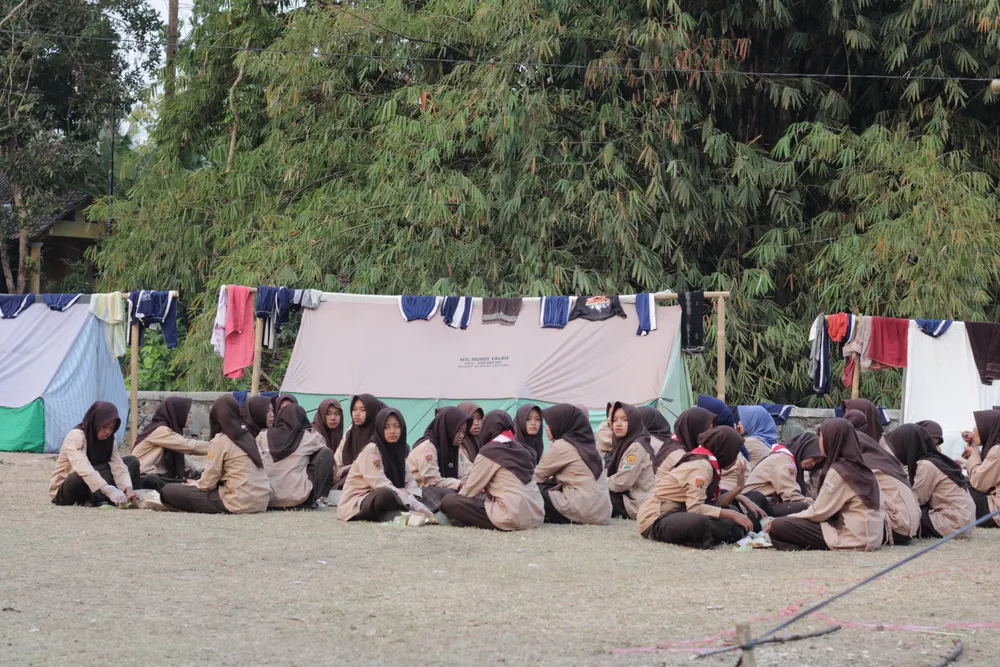 Peserta pramuka duduk berkelompok di lapangan dengan deretan tenda di belakang mereka